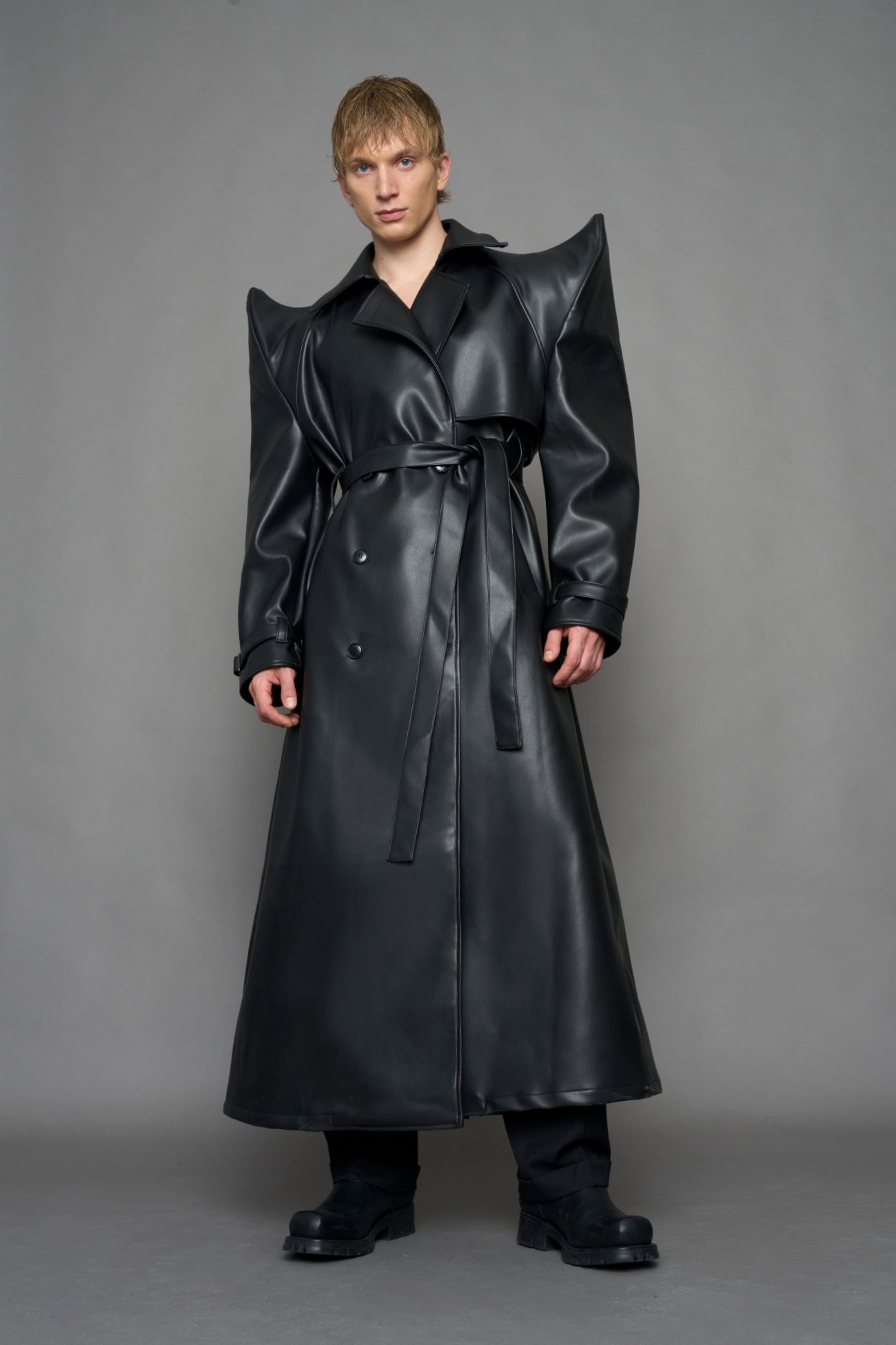 model wearing black vegan leather trench coat with sharp shoulder design