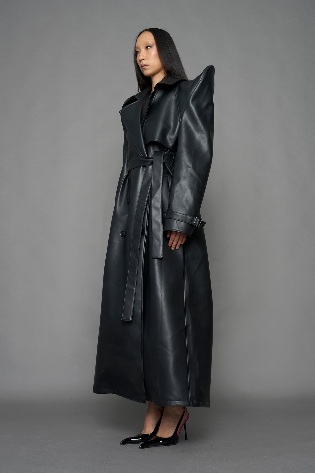 model wearing black vegan leather trench coat with sharp shoulder design
