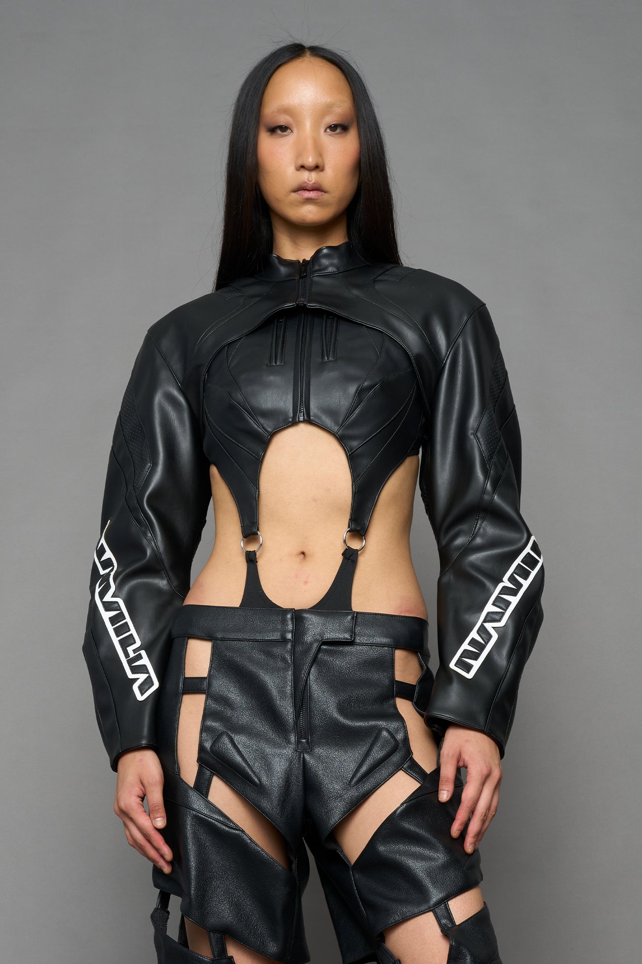 A model wearing a black faux-leather futuristic bodysuit with a high collar