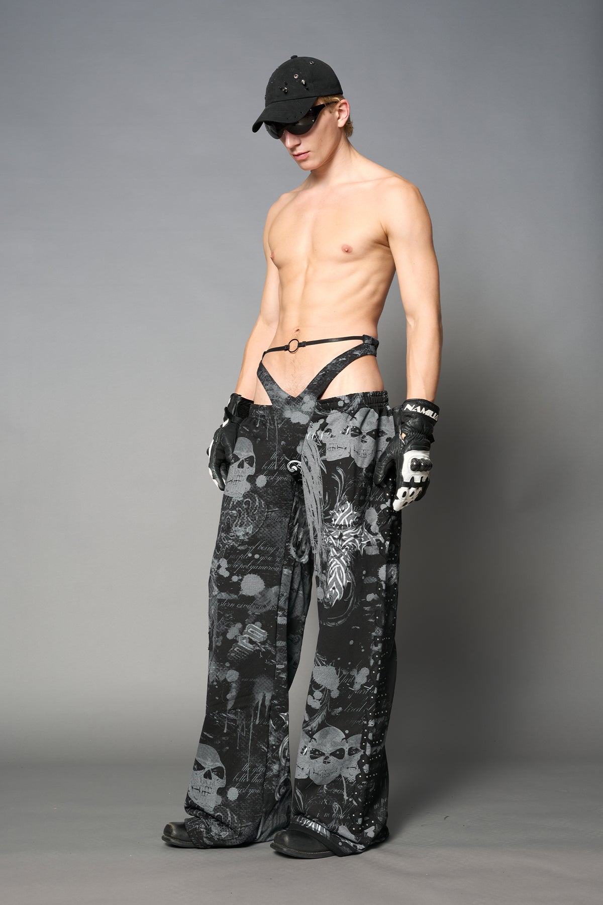Model wearing low-rise black print wide-leg pants featuring a V-shaped waistband and detachable thong strap detail.