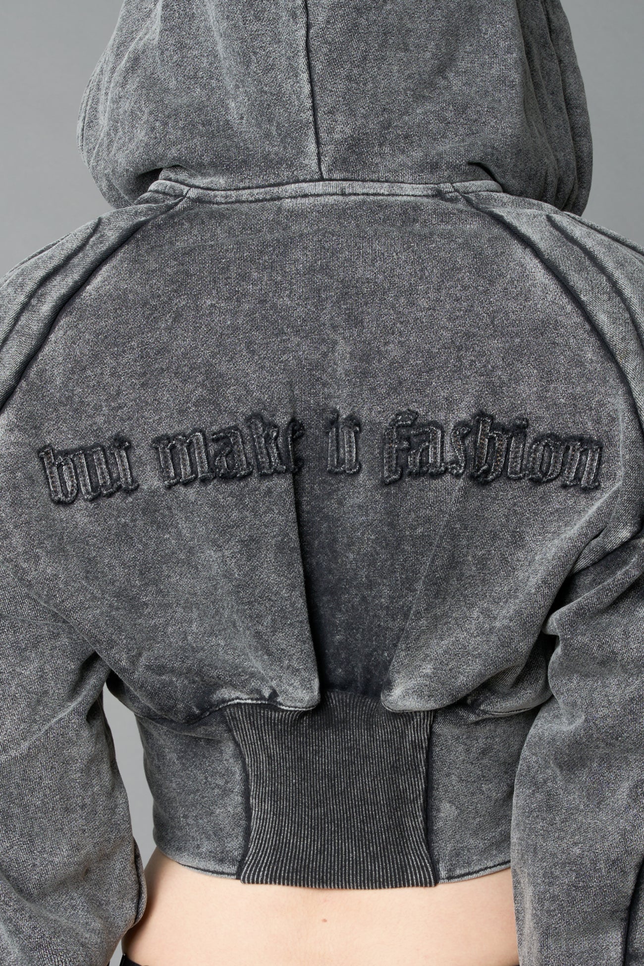 model in a washed-black cropped hoodie featuring structured corset-style paneling embroidered across the chest in tonal black