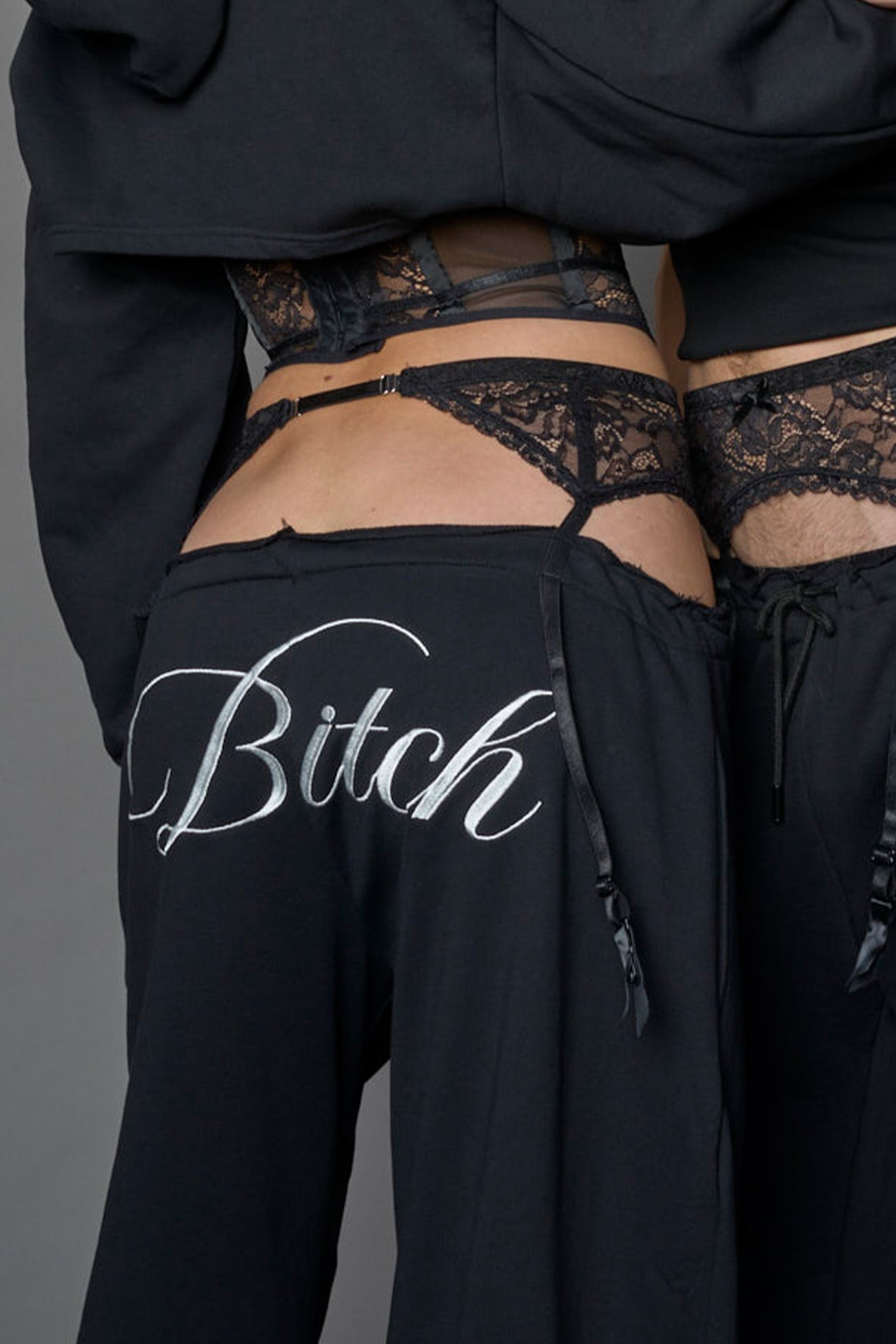detail of a black low waist jogger with a lace suspender belt and statement embroidery