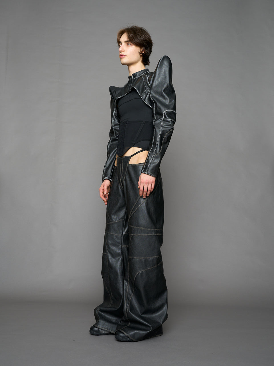 Model wearing a black vegan leather spike shoulder bolero jacket with cut-out design on a gray background