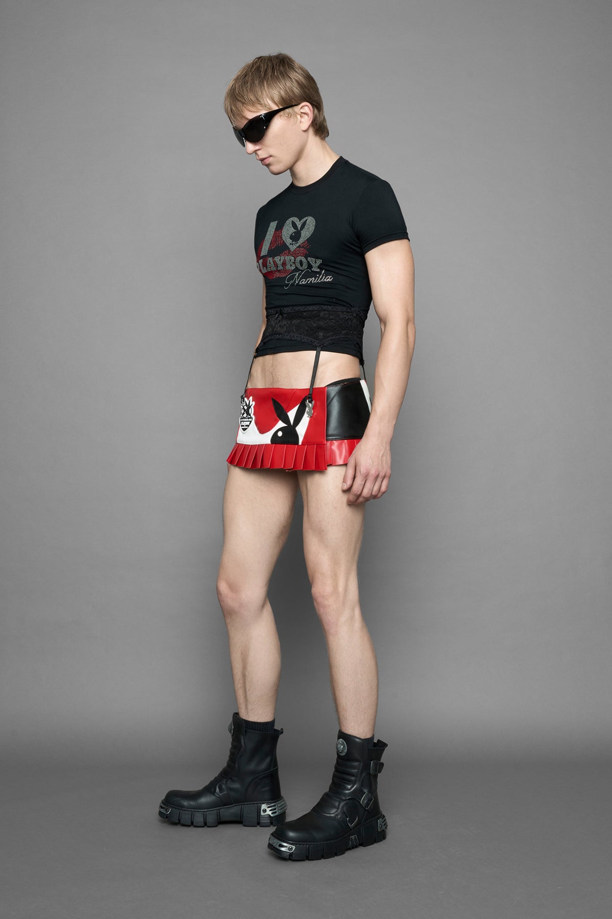 model wearing a black short-sleeve graphic t-shirt with rhinestone embroidery of red lip print and silver 'I <heart> PLAYBOY' design. T-Shirt has a lingerie black lace garter with suspender with metal silver Bunny Heads attached.