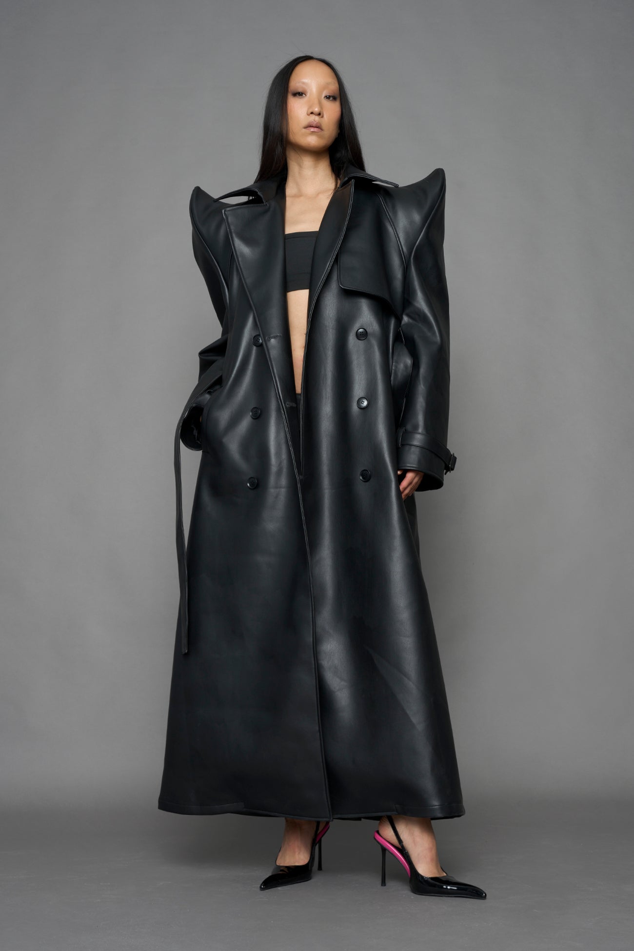 model wearing black vegan leather trench coat with sharp shoulder design
