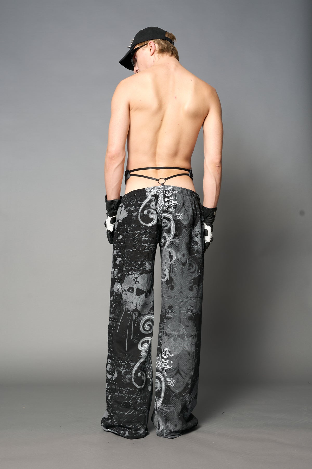 Model wearing low-rise black print wide-leg pants featuring a V-shaped waistband and detachable thong strap detail.