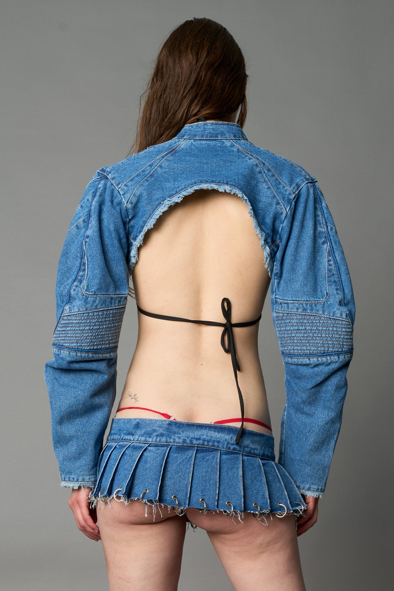Model in ultra-cropped blue washed denim bolero jacket with front zipper, raw frayed edges, choker neckline, and sculpted biker sleeves
