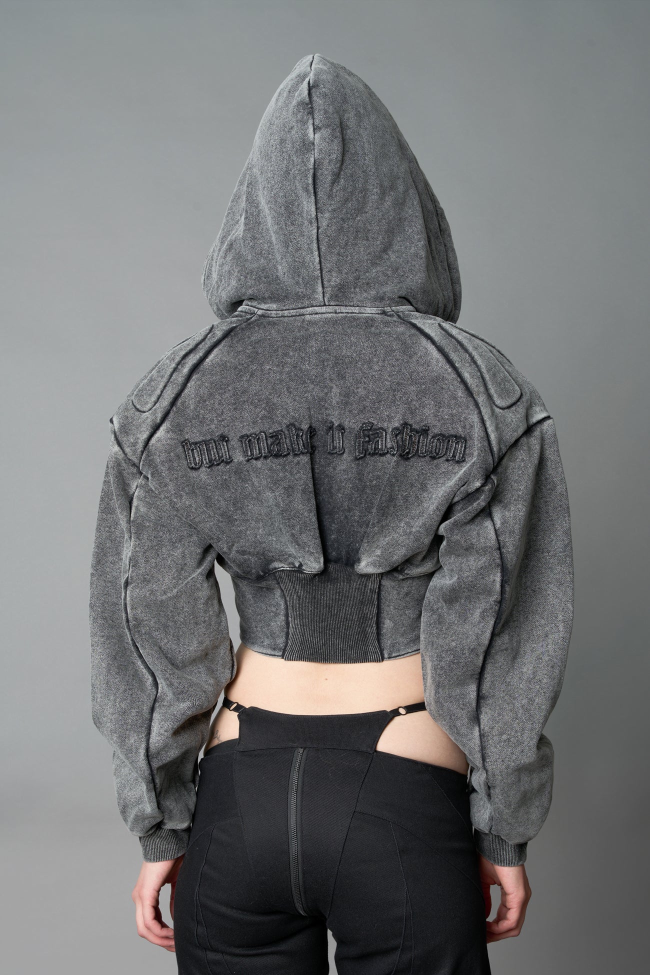 model in a washed-black cropped hoodie featuring structured corset-style paneling  embroidered across the chest in tonal black