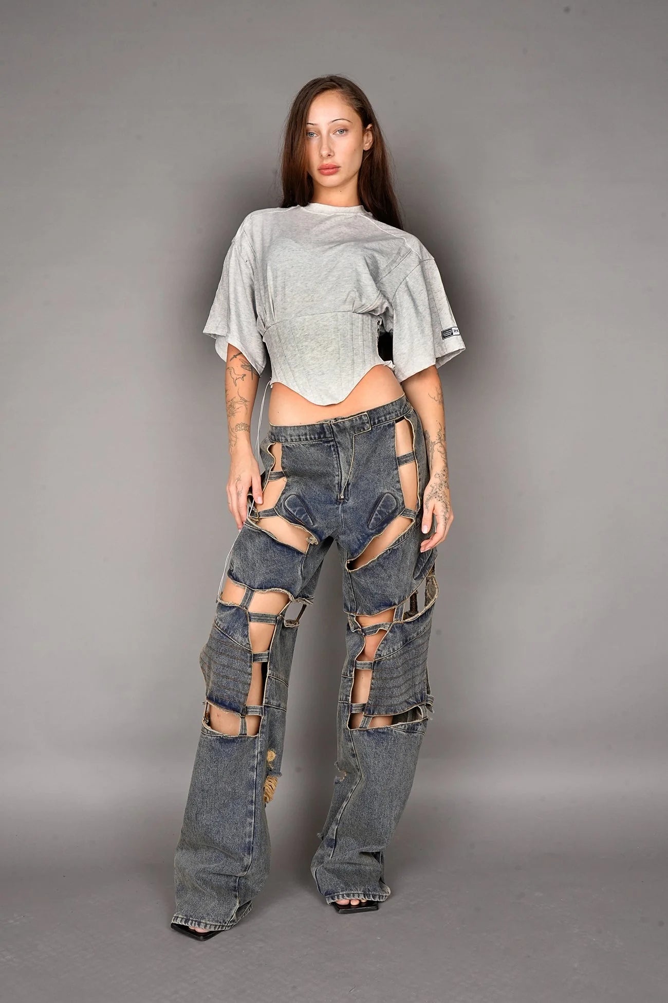 Person wearing a grey crop top and ripped jeans on a gray background