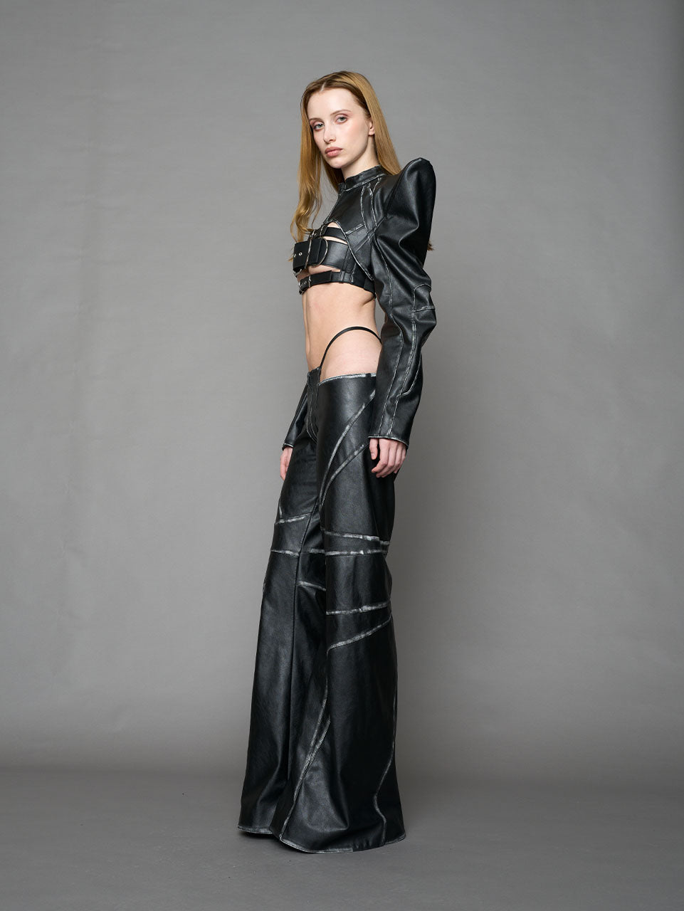 Model wearing a black vegan leather spike shoulder bolero jacket with cut-out design on a gray background