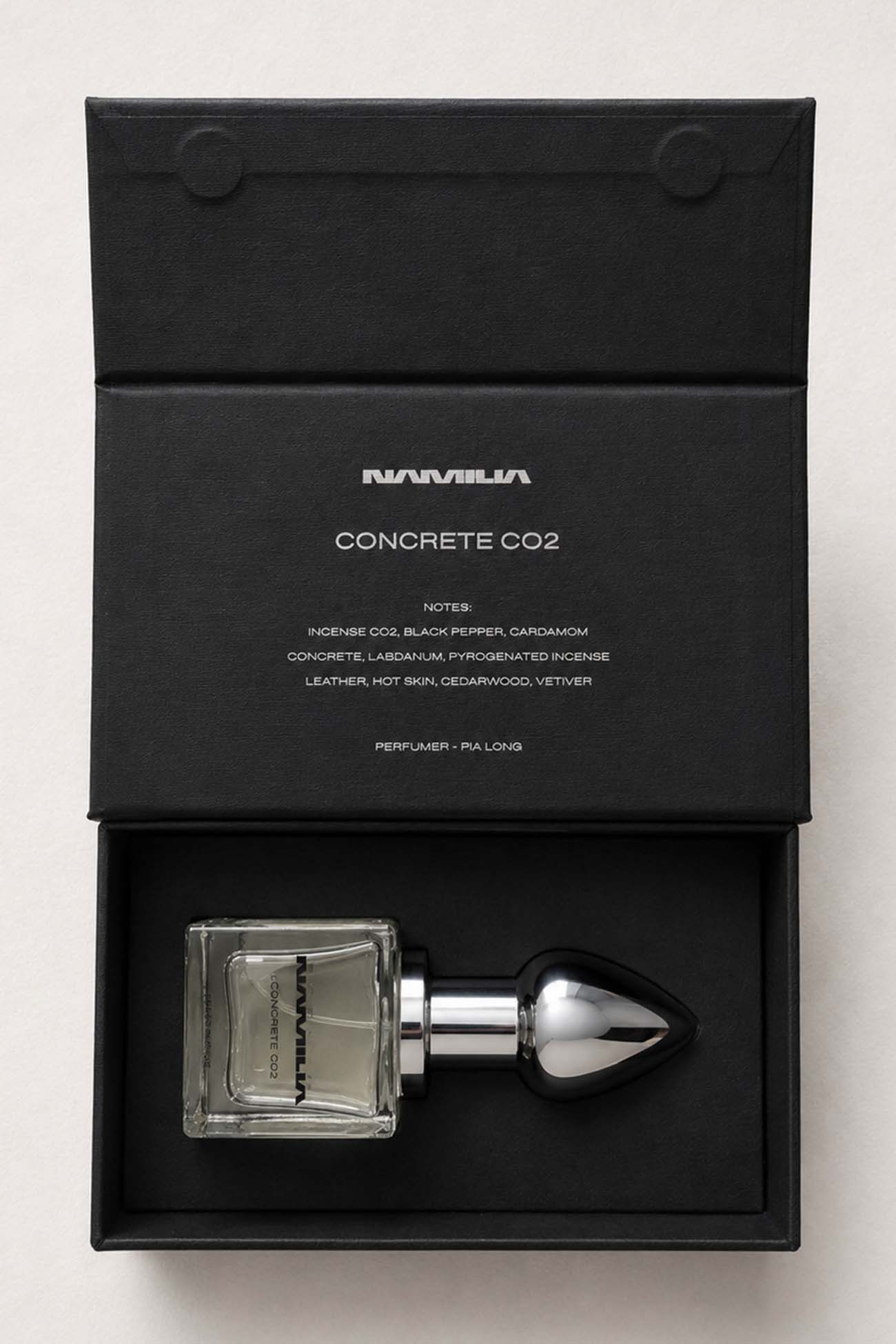 A bottle of Namilia Concrete CO2 Eau de Parfum with a large reflective black plug-shaped cap