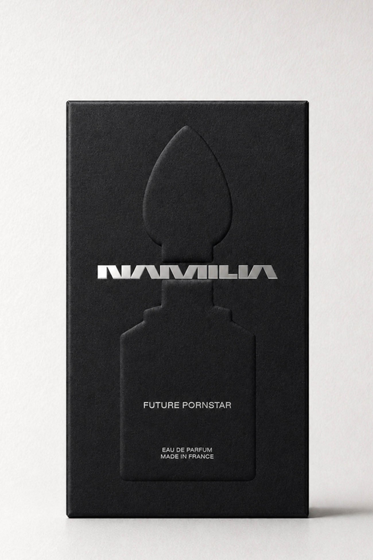 A bottle of Namila  Eau de Parfum with a large reflective plug-shaped cap inside the box