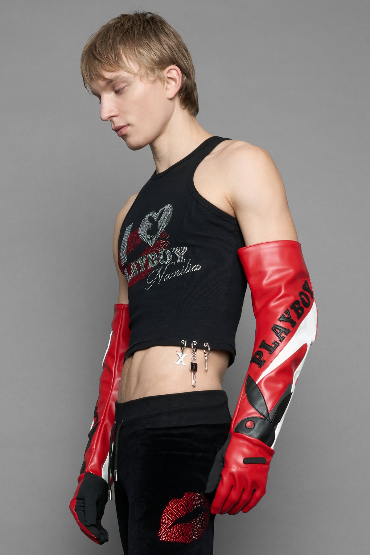 A model wearing a black halter crop top with red and silver 'I <heart> PLAYBOY Namilia' graphic, paired with black pants featuring a red lip print