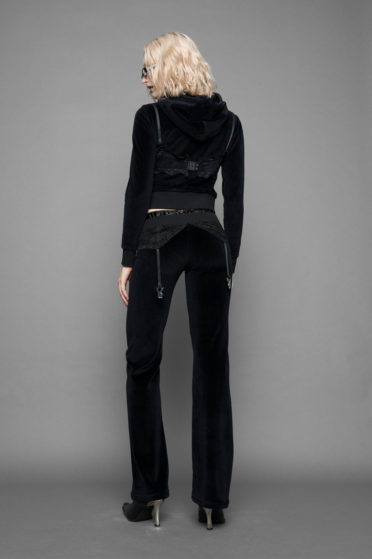 A female model wearing black velvet tracksuit pants with a lingerie black lace garter and suspenders with metal silver Bunnys 
