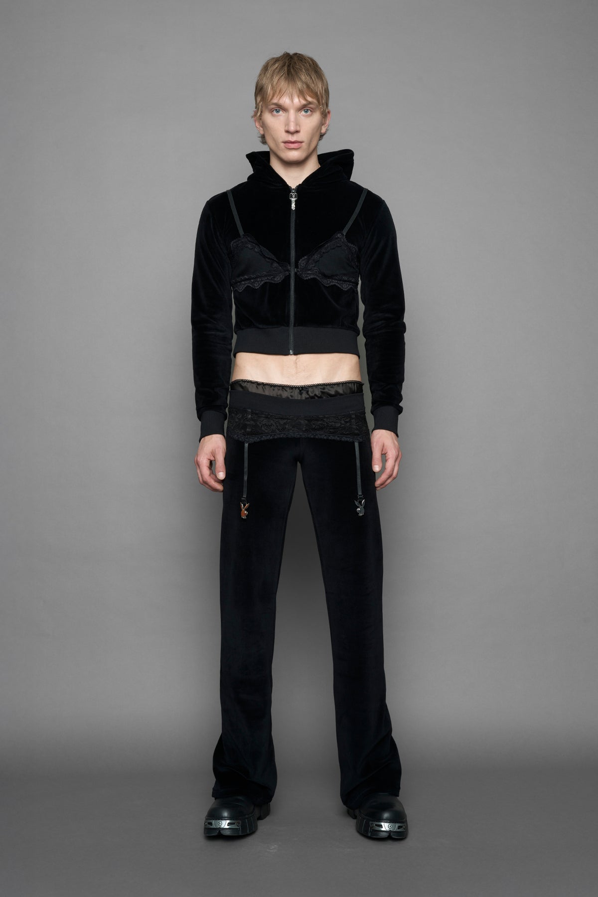 A female model wearing black velvet tracksuit pants with a lingerie black lace garter and suspenders with metal silver Bunnys 