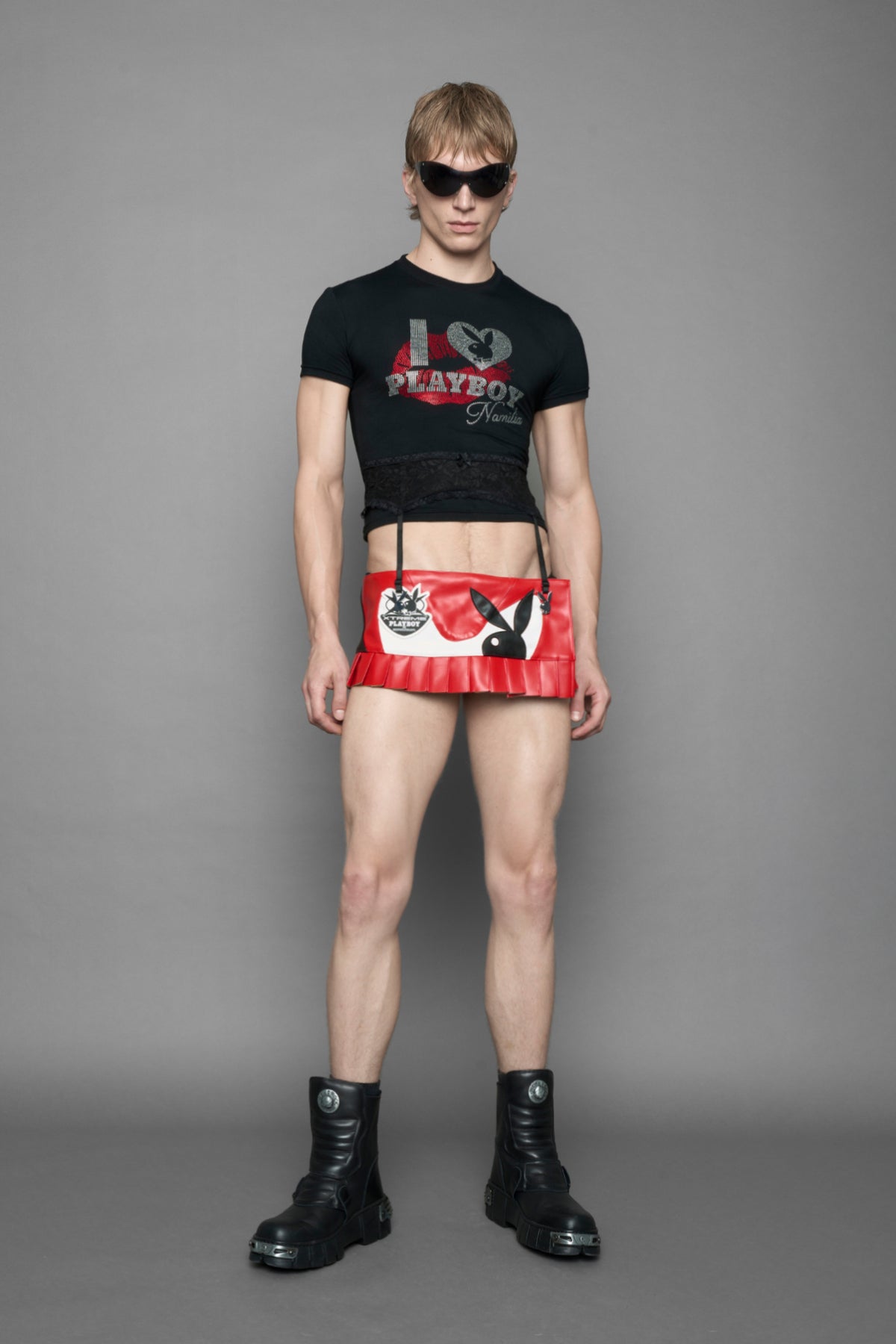 model wearing a black short-sleeve graphic t-shirt with rhinestone embroidery of red lip print and silver 'I <heart> PLAYBOY' design. T-Shirt has a lingerie black lace garter with suspender with metal silver Bunny Heads attached.